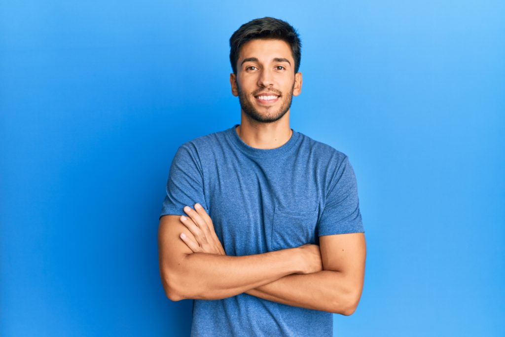 young handsome man wearing casual tshirt blue background happy face smiling with crossed arms looking camera positive person